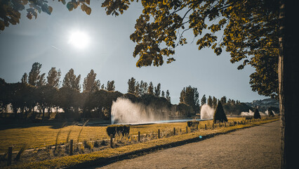 Sunlit fountains and trees in Borely Park, Parc Borély, Marseille, Marseilles, France. Warm summer afternoon with golden light and elegant landscape scenery