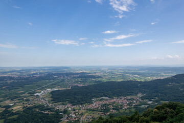 Drone panorama of the Ivrea Morainic Amphitheatre seen from Brosso, Val Chiusella, Italy, showing lush green plains, woods, and scattered villages under clear sky, high drone shot, slow motion