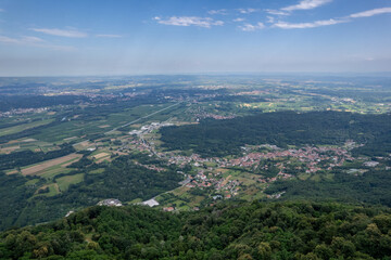 Drone panorama of the Ivrea Morainic Amphitheatre seen from Brosso, Val Chiusella, Italy, showing lush green plains, woods, and scattered villages under clear sky, high drone shot, slow motion