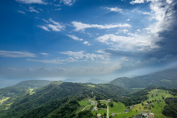 Fototapeta premium Drone panorama of the Ivrea Morainic Amphitheatre seen from Brosso, Val Chiusella, Italy, showing lush green plains, woods, and scattered villages under clear sky, high drone shot, slow motion