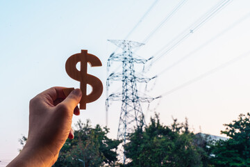 Businessman's hand holding a symbol Dollar with electric pole background, concept of electricity bills, electricity generation, public utility bills.