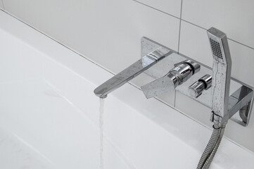 A bathtub in the bathroom secured with white silicone and a clean chrome faucet with a shower head
