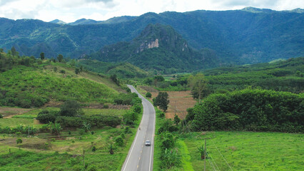 Aerial view of car running on the road among the forest and mountains