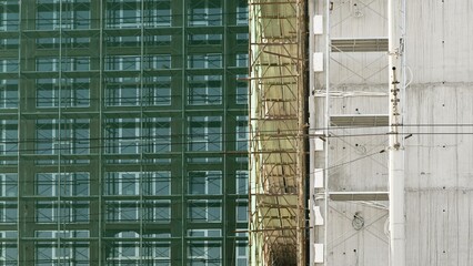 High-rise building under construction with green mesh safety netting, scaffolding platforms, and exposed concrete surfaces during facade installation or renovation work.
