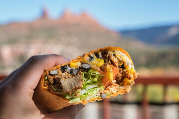 Close-up of hand holding burrito against mountains and sky in Sedona, Arizona, USA