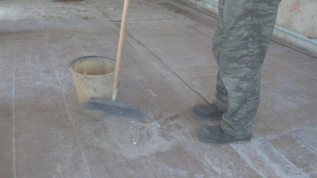 Man sweeping dust and debris on the floor of an empty, abandoned room using a broom or mop. Neglected space shows signs of decay and wear