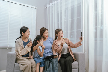 Happy Asian family sitting on cozy living room sofa, bonding and smiling while enjoying time...