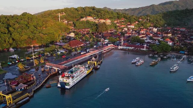 A ferry rests in Padang Bai Port Bali as drone footage captures the coastline blue water and hills surrounding this busy harbor filled with tropical charm and local boat activity.