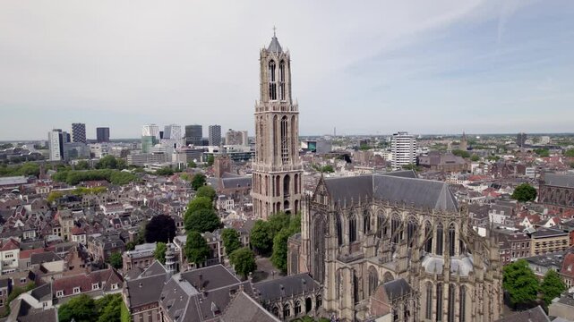 Slow ascending aerial movement showing gothic architecture of cathedral and De Dom church tower in historic city center of Utrecht with Dutch high rise buildings in background