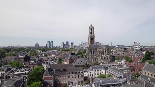 Descending aerial revealing historic city center buildings beneath Utrecht gothic architecture of diocese ambulatory with modern high rise buildings on the horizon behind