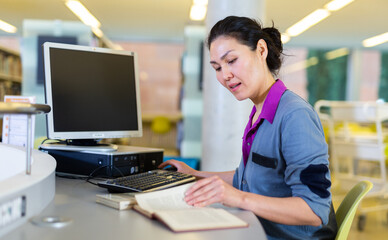 Woman engaged in self-education using pc for searching information in public libraryary