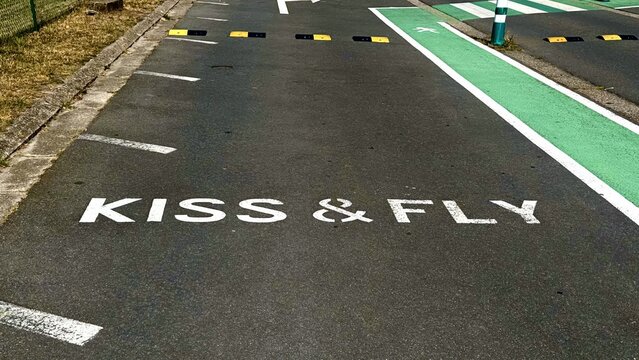 White Kiss and Fly inscription on road near green bike lane and speed bumps at airport drop-off zone

