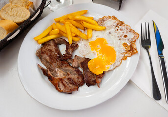Cooked tender veal with fried egg and French fries. Serving a Spanish meat dish on a white plate