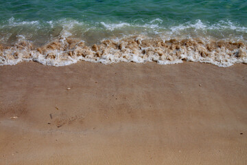 Gentle sea waves washing over golden sand on a tropical beach. A calm and natural shoreline close-up, perfect for backgrounds and vacation themes.