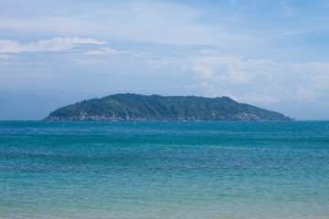 A distant view of a green Cham Island in Vietnam surrounded by turquoise sea under a partly cloudy...