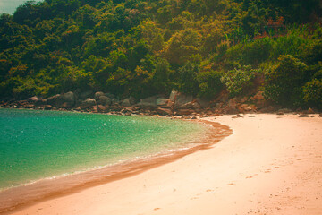 Tropical beach with soft sand and emerald water surrounded by lush green hills, captured in Cham...