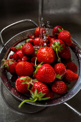 Fresh strawberries rinsing in a metal colander under a stream of water in a kitchen sink.