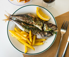 Grilled scomber with herb sauce served with vegetable garnish of fried potatoes and lemon slice