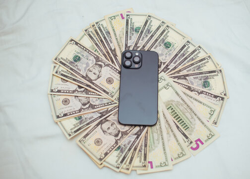 An Android smart phone place on the top spread of multiple dollars cash money on a white surface