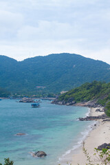 Scenic coastal view of Cham Islands with fishing boats, tropical mountains and a person walking along a deserted beach.