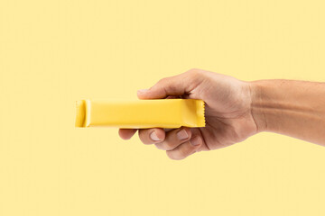 Male hand holding yellow snack bar mockup isolated on yellow background cutout