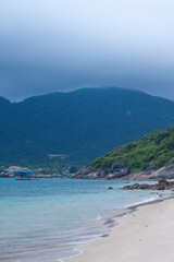 Tropical beach with soft sand and emerald water surrounded by lush green hills, captured in Cham Islands, Vietnam.
