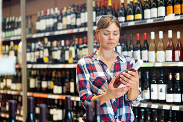 Portrait of young woman visiting winehouse in search of bottle of good wine