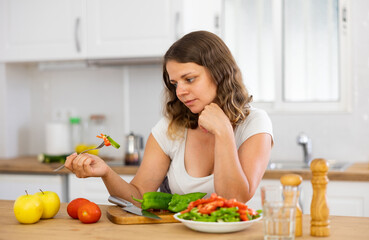 Portrait of thinking young woman during cutting vegetable on kitchen, looking with disgust and dislike