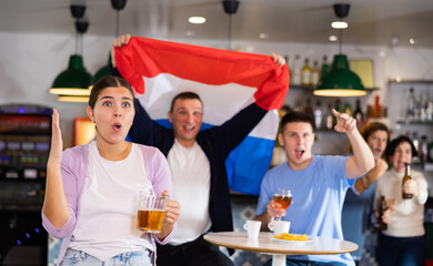 Fans with flag of Netherlands celebrate victory of their favorite team in a beer bar