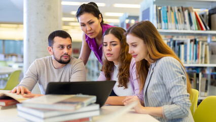 Group of enthusiastic young adult female and male colleagues working together in public library,...