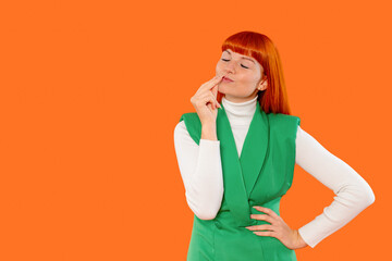 Young woman with red hair in green attire thinks deeply against an orange backdrop during a...