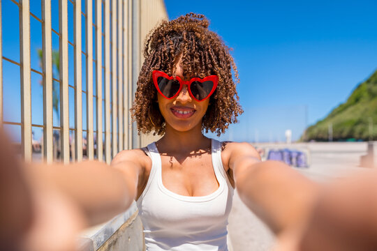 Young woman taking a selfie wearing heart shaped sunglasses on beach boardwalk