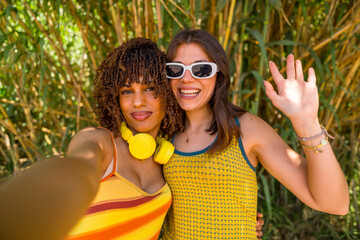 Two smiling young women taking a selfie and waving in a bamboo forest