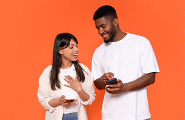 Young couple sharing a light moment while looking at their smartphones against an orange background