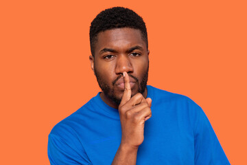 Person making a shushing gesture while wearing a blue shirt against a bright orange background...