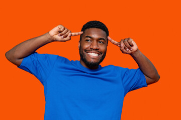 Young man expressing joy and confidence with playful gestures against a vibrant orange background...