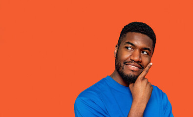 Young man in blue shirt pondering a thought against a vibrant orange background in a casual indoor...