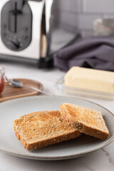 Close-up of two golden toasts on a grey plate, with butter and toaster. Frontal composition with soft background. Concept of simple and everyday breakfast