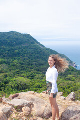 Naklejka premium Smiling woman posing with wind in hair and coastal view. 