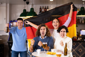 Smiling man and woman with Germany flag drinking alcohol and having conversation on party in nightclub