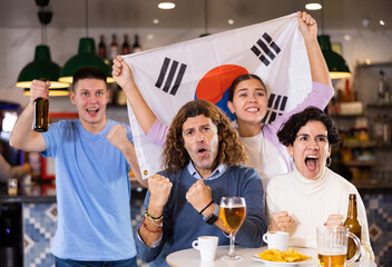 Company of young adult fans supporting team of South Korea with state flag while resting in sports bar with beer