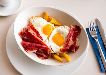 Plate of appetizing hearty breakfast of fried eggs with slices of delicious bacon and French fries