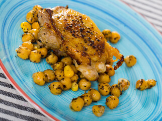 Dish of tasty fried chicken thighs served with cheakpea at plate on table