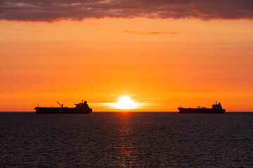 Silhouettes of two cargo ships at anchor in the Baltic Sea against a golden sunset. Evening seascape off the coast of Estonia.