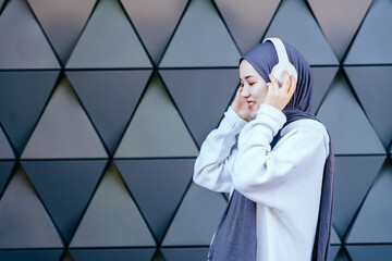 Muslim woman listening to music with headphones in modern urban setting