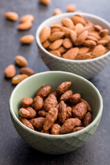 Almond nuts coated in sugar and honey in bowl on black table.