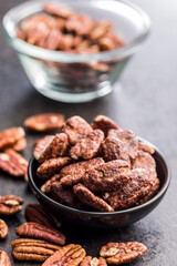 Pecan nuts coated in sugar and honey in bowl on black table.