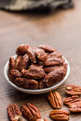 Pecan nuts coated in sugar and honey in bowl on wooden table.