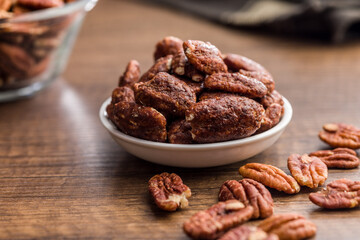 Pecan nuts coated in sugar and honey in bowl on wooden table.