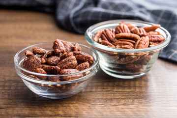 Pecan nuts coated in sugar and honey in bowl on wooden table.